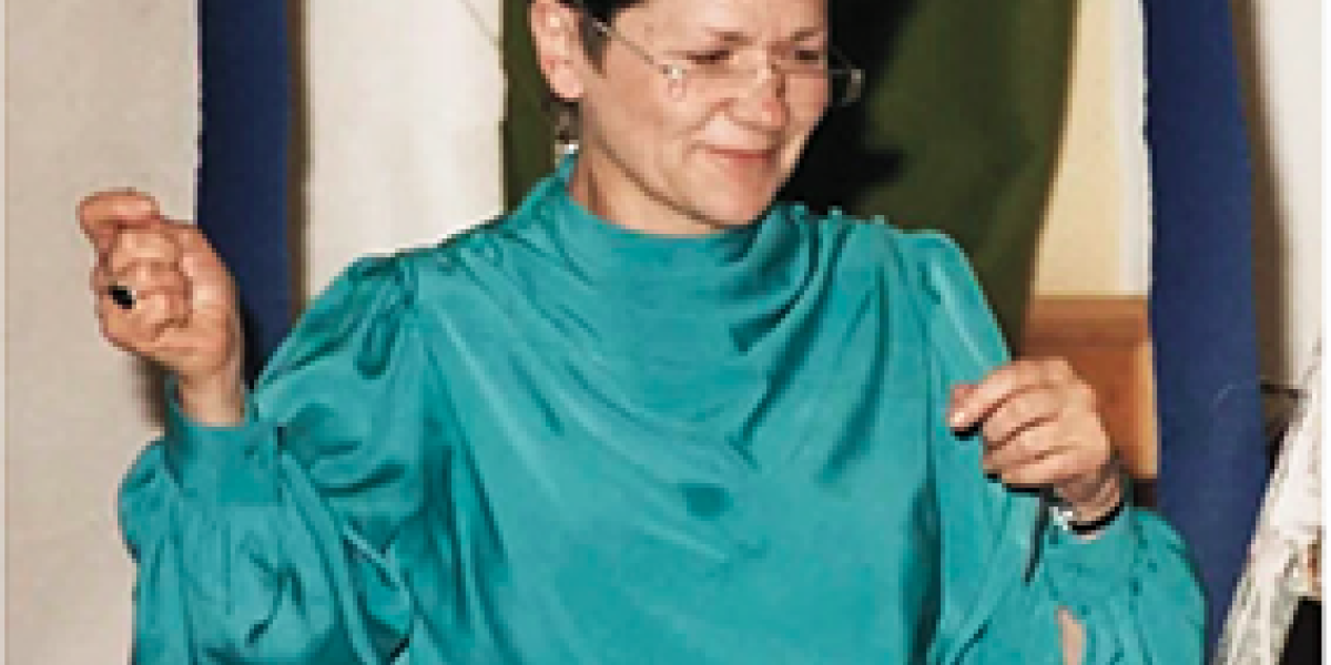 Traude trägt eine grünes Kleid und eine Brille